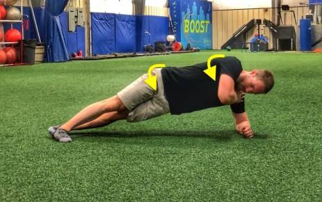 Dr. Aaron Horschig apoiado de lado pelos joelhos e cotovelos em chão de grama sintética em posição do full side plank com rolamento do core