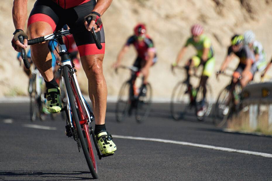 Pelotão de atletas de ciclismo, mantendo uma alta cadência durante subida na estrada.